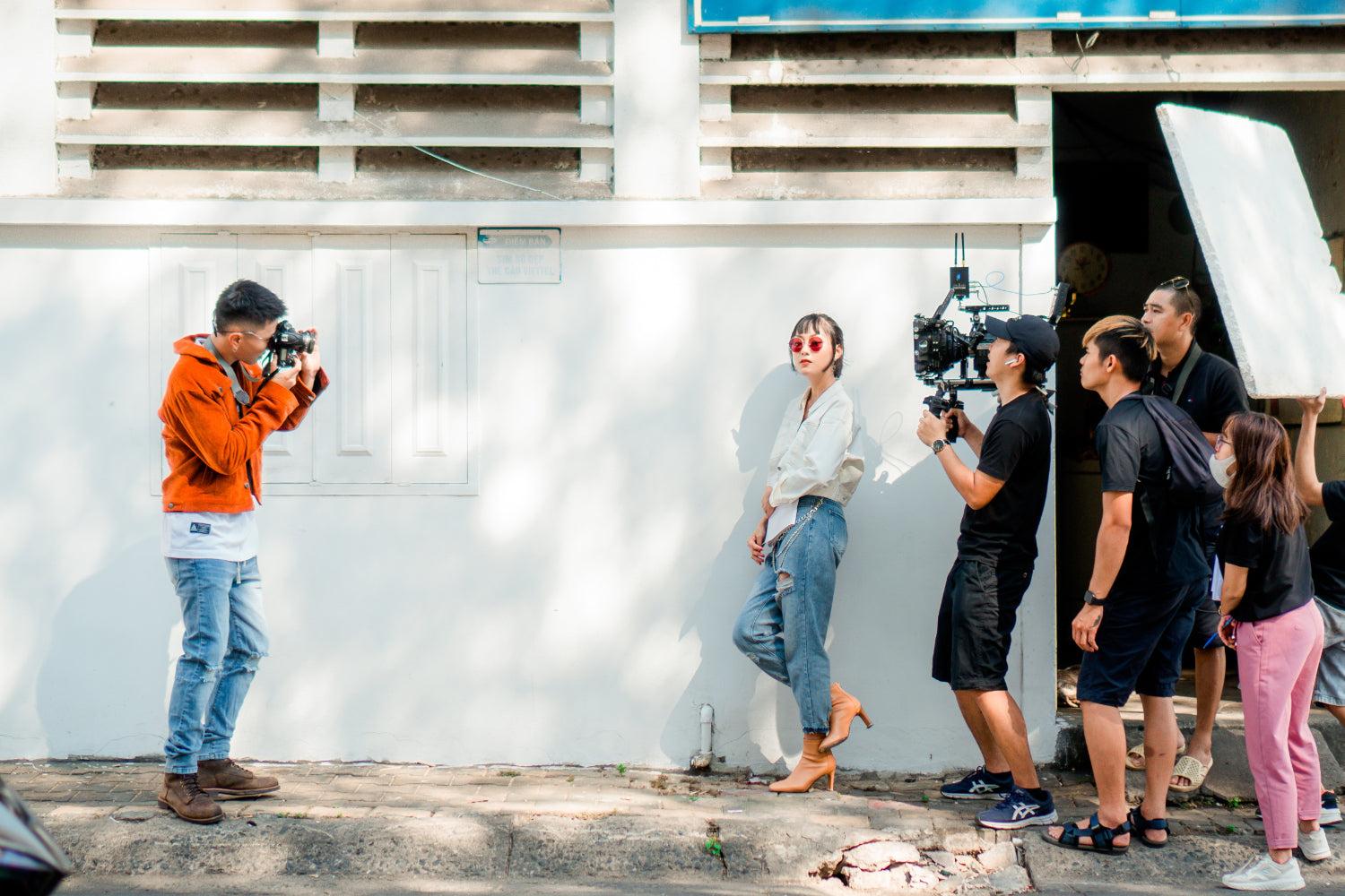 一名摄像师正在拍摄模特摆姿势的画面，而其他制作人员则在画面外协助